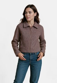 Bruine wollen cropped jasje met een kraag, een rits aan de voorkant en zijzakken, gecombineerd met blauwe jeans. De stof heeft een gestructureerde afwerking.