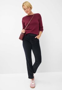Bordeaux trui gecombineerd met donker zwarte broek en roze sneakers. Het model draagt een kleine bordeaux crossover tas. Eenvoudig ontwerp, casual stijl.