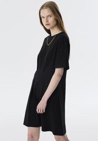 Schwarzes kurzes Kleid mit kurzen Ärmeln aus glattem Stoff, das eine lässige Passform, subtile Seitennaht und eine goldene Kettenhalskette als Accessoire bietet.