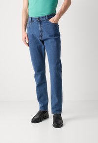 Blå denimjeans med lös passform, med knappstängning, framfickor och platta sömmar. Bärs med svarta loafers.