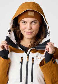 Brown and white waterproof jacket with a hood, featuring black accents, adjustable drawstrings, and logo detailing on the chest.