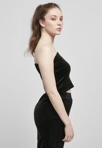 Un crop top en velours noir associé à un pantalon taille haute assorti ; texture lisse, design ajusté et silhouette cropped.