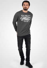 Gray long-sleeve sweatshirt with white text stating "New York City Superior" and dark jeans with a distressed design. Black sneakers.