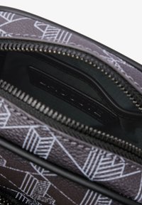 Bolso con cremallera que presenta un exterior texturizado negro con patrones geométricos blancos, revelando un interior suave y oscuro con una etiqueta de marca.