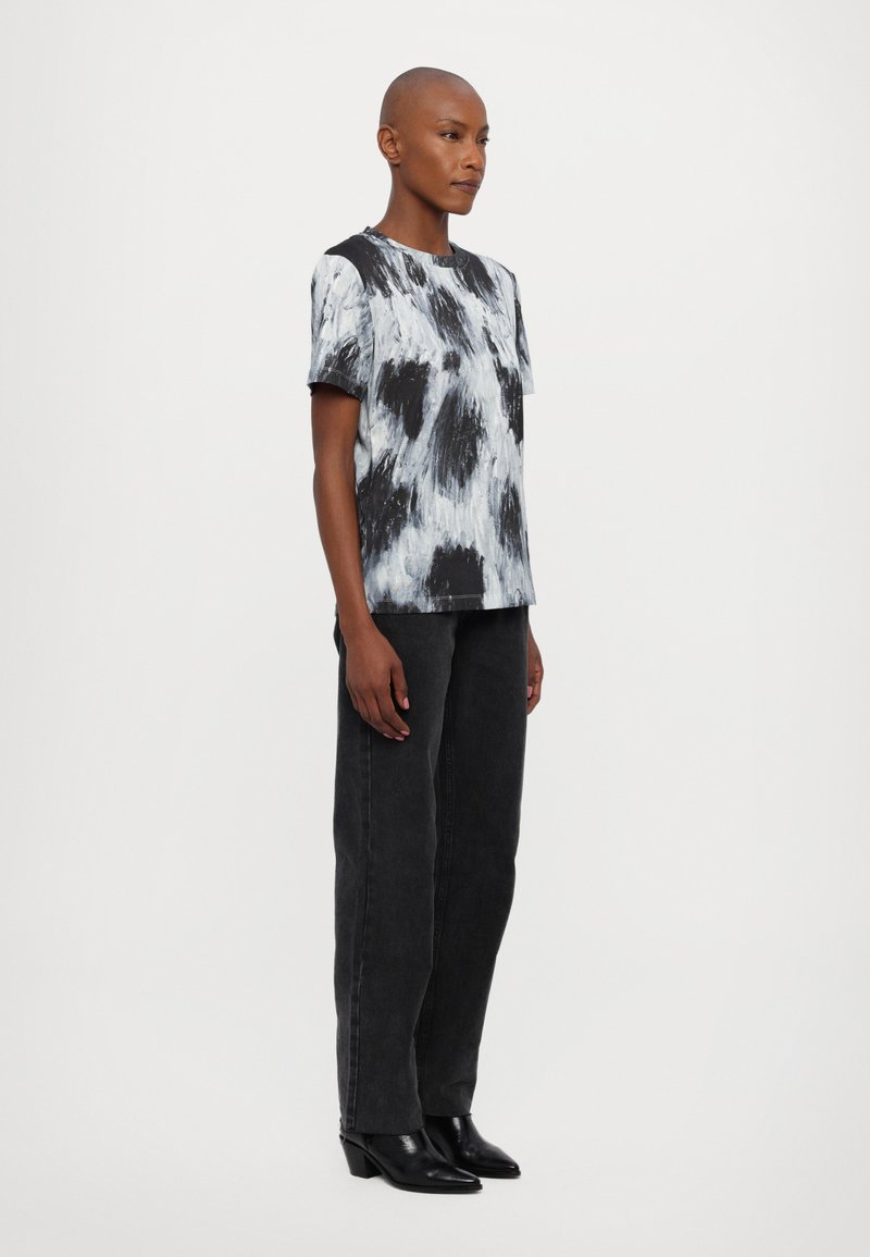 T-shirt à manches courtes en tie-dye noir et blanc avec un col rond, associé à un jean noir taille haute et des bottines noires.