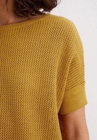 Top amarillo de punto con un patrón suelto y abierto, escote amplio y mangas cortas acanaladas. Tejido ligero y texturizado.
