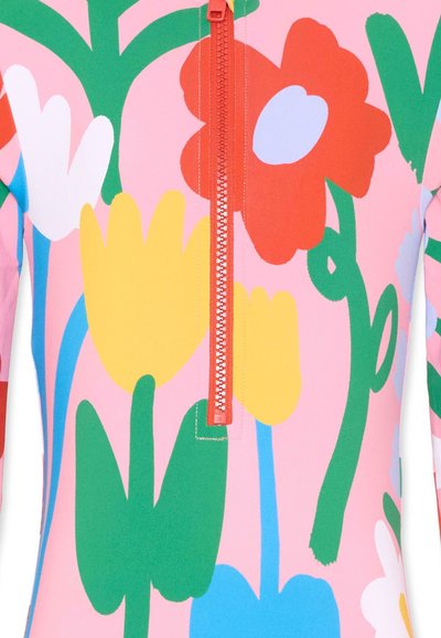 Motif floral éclatant avec de grandes fleurs rouges, jaunes, blanches et bleues, ainsi que des tiges vertes sur un tissu rose, avec une fermeture éclair centrale orange.