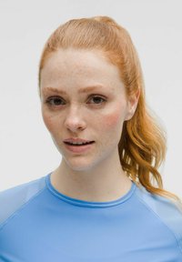 Hele sinise, fitneeritud sporttop, ümmarguse kaelusega ja siledast tekstuurist. Modellil on ponisaba ja tedretäppidega nägu ning neutraalne ilme.