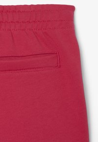 Pantalones de chándal rojos con un acabado texturizado, cintura elástica y un pequeño bolsillo en la parte posterior. La tela parece suave y transpirable.