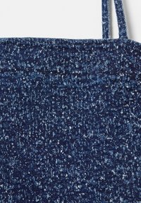 Denimová tkanina v tmavě modré barvě s texturovaným vzorem a světlejšími skvrnami, přišité okraje a tenké popruhy. Vhodné pro různé styly.