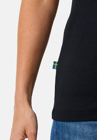 Black t-shirt made of cotton, featuring a blue and yellow Swedish flag tag on the left side. Straight hem with slight stretch.