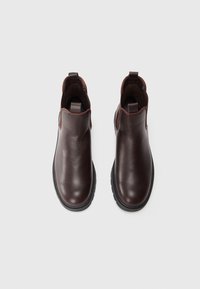 Botas de tobillo de cuero marrón con una textura suave. Cuentan con una suela de goma negra y costados elásticos para facilitar su uso sin cordones.