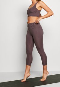 Two-piece activewear set in muted mauve. The sports bra has a scoop neck and ruching, while the leggings are high-waisted with side pockets.