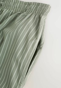 Grün gestreifte Hose mit elastischem Bund und Seitentaschen, aus leichtem Stoff mit glatter Textur gefertigt.