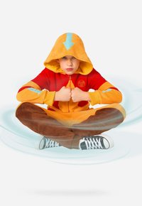 Oranž punase ja siniste aktsentidega fliisist kombinesoon. Kapuutsil on allapoole suunav nool. Pruunid pidžaamapüksid. Must-valged kõrged tossud.