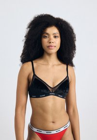 Black velvet bralette with sheer mesh accents and HUGO logo at the band. Paired with red underwear featuring a white logo waistband.
