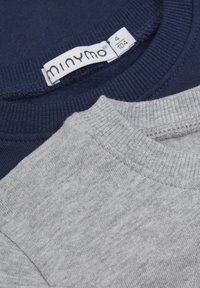 Twee truien: één marineblauw, de andere lichtgrijs. Beide hebben een geribde halslijn en een zachte katoenen textuur. Het label toont maat 4 en het merk "minymo."