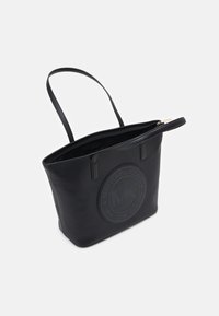 Sac fourre-tout en cuir noir avec un logo en relief rond d'un côté, surface texturée, anses doubles et design ouvert en haut.