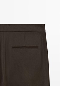 Tessuto marrone scuro con una singola tasca a filetto orizzontale e cuciture visibili nella parte superiore posteriore di pantaloni su misura.