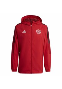 Chaqueta ligera roja con capucha, que presenta detalles y rayas en negro. Incluye el logo de Manchester United y la marca Adidas en el pecho.