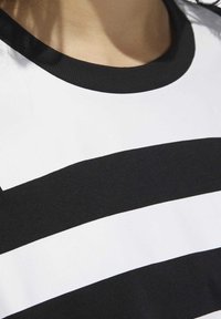 Svartvitt randig skjorta med svart ribbad rund hals, med breda horisontella ränder i samma bredd och en slät bomullstextur.