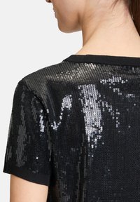 Schwarzes Pailettenoberteil mit Rundhalsausschnitt und kurzen Ärmeln. Die Textur ist reflektierend mit einer dichten Anordnung von kleinen, runden Pailletten.