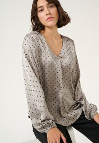 Silky, light gray blouse with a V-neck, long sleeves, and black polka dots. Features elasticized cuffs and a relaxed fit.