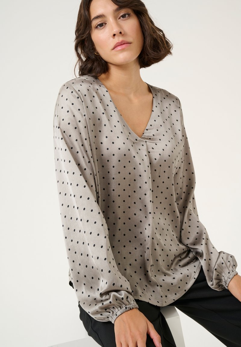 Silky, light gray blouse with a V-neck, long sleeves, and black polka dots. Features elasticized cuffs and a relaxed fit.