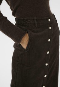 Brown corduroy skirt featuring vertical ribbing, side pockets, and a front button closure with silver hardware. Textured fabric.