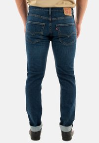 Jeans in denim blu con una vestibilità dritta, caratterizzati da un logo in pelle sulla parte posteriore della vita e tasche doppie cucite. Cuffs arrotolati.