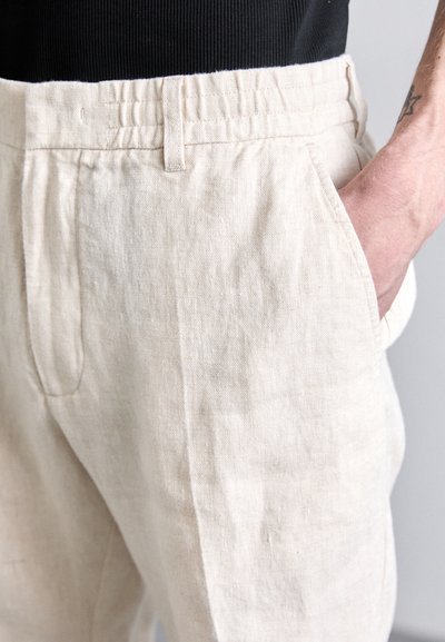 Beige Leinenhosen mit entspannter Passform, ausgestattet mit Seitentaschen und einem Bund aus gerafftem Gummi. Die Textur wirkt leicht und weich.