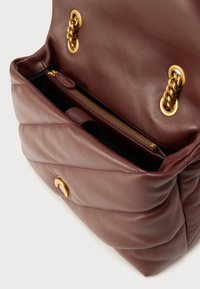 Καφέ δερμάτινη τσάντα χειρός με καπιτονέ σχέδιο, που διαθέτει χρυσές αλυσίδες, τσέπη με φερμουάρ και υφασμένο εσωτερικό.