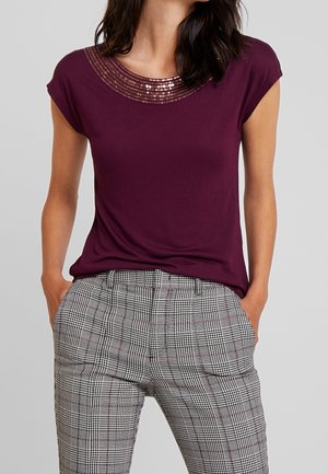 Camiseta burdeos con cuello redondo de lentejuelas, mangas cortas, combinada con pantalones de cuadros grises con patrones en blanco y negro.