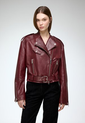 Bordeaux leren motorjack met een riem in de taille, reverskraag en zilveren ritsen; voorzien van schouderepauletten en een opvallende textuur.