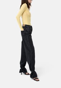Gelbes Langarmoberteil kombiniert mit weiten schwarzen Jeans aus Denim. Die Jeans haben einen rohen Saum und hautfreie schwarze High Heels mit dünnen Riemen.