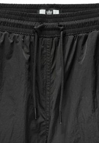 Schwarze Shorts aus leichtem, strukturiertem Stoff. Verfügt über einen elastischen Bund mit Kordelzügen und ein kleines Logo an der Oberseite.