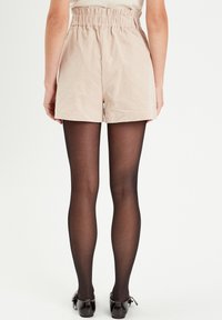 Beige corduroy shorts met een elastische tailleband, gecombineerd met doorschijnende zwarte panty's en donkere lakleren schoenen.