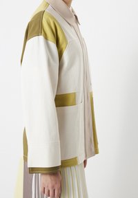 Veste en coton présentant un mélange de panneaux crème, vert clair et beige. Comprend un col et des poches avant avec des coutures contrastantes.
