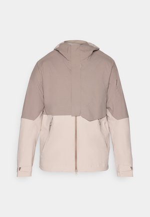 Chaqueta ligera bicolor con un cuerpo beige suave y mangas de un tono topo más oscuro. Cuenta con una capucha, cremallera frontal y puños ajustables.
