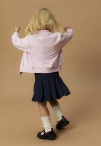 Felpa rosa chiaro con una vestibilità morbida, abbinata a una gonna plissettata blu scuro. Calze bianche a costine e scarpe scure completano l'outfit.