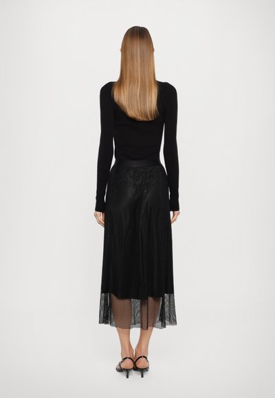 Top preto de manga longa e saia transparente de malha preta com um padrão de pontos, apresentando uma cintura ajustada e uma bainha em camadas.