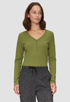 Langdurige mouw, V-hals top in olijfgroen ribbelstof met een vijfknopenpat. Gepaard met grijze, gestructureerde broek met een trekkoord.