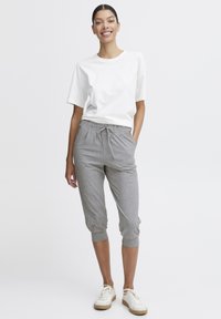 Hvit kortermet t-skjorte kombinert med grå, avkuttede joggebukser med elastisk liv og snøring. Modellen har på seg lette sneakers.