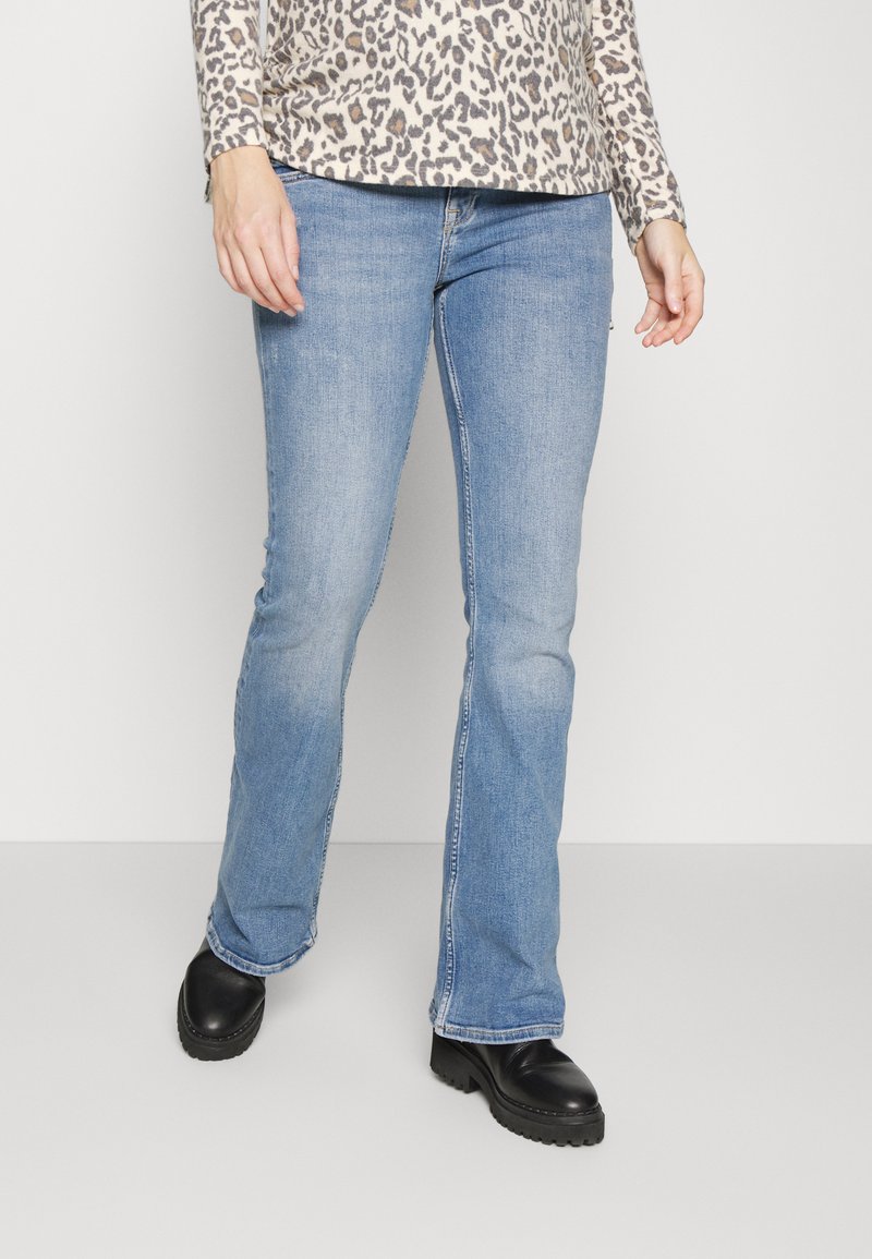 Jeans de ganga azul claro, com corte flared, apresentando um design clássico de cinco bolsos e um desbotado subtil, combinados com calçado preto.