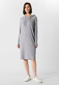 Szara, prążkowana sukienka-hoodie z długimi rękawami, z frontową kieszenią i sznurkami do regulacji. Połączona z białymi trampkami, aby uzyskać casualowy wygląd.