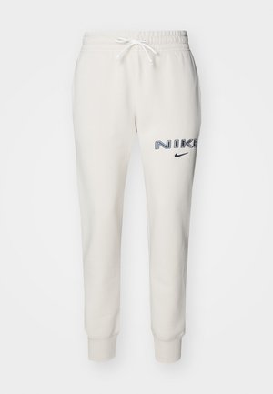 Pantaloni sportivi beige chiaro realizzati in tessuto morbido, con cintura elastica e cordoncino, polsini a costine e marchio Nike blu navy sulla coscia sinistra.