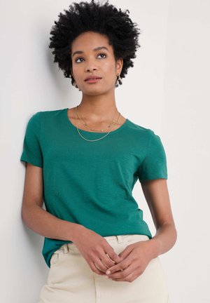 Groene kortemouw T-shirt met een ronde hals, gemaakt van zachte stof. Gepaard met crèmekleurige broek en gelaagde gouden kettingen.