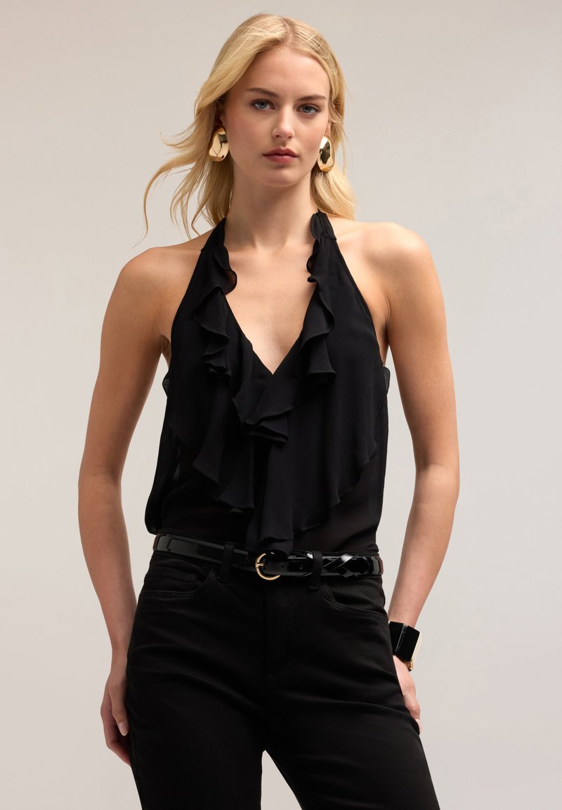 Black halter top with ruffled design, made of lightweight fabric. Paired with black jeans and a glossy belt featuring a round buckle.