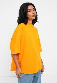 Oransje oversized bomull t-skjorte med høy hals og korte ermer, med en avslappet fasong og glatt tekstur.