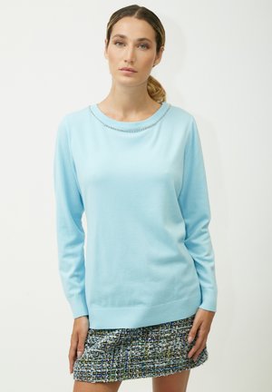 Pull en maille bleu clair à manches longues et décolleté arrondi, avec un détail de chaîne décoratif le long du col. Coupe décontractée.
